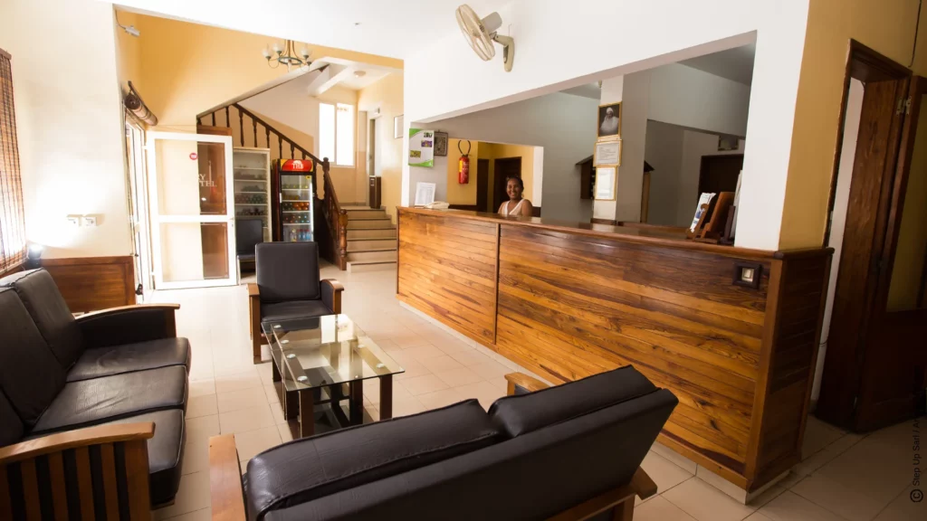 Espace réception chaleureux de Anjary Hôtel à Majunga avec un comptoir en bois, une réceptionniste souriante et un coin salon confortable.