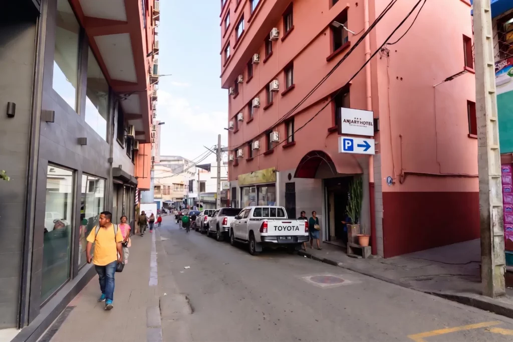 Voitures garées et enseigne d'Anjary Hôtel avec parking à Antananarivo centre-ville