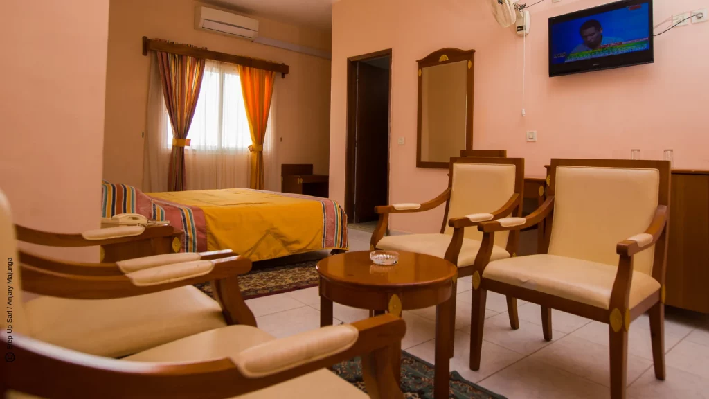 Chambre spacieuse et lumineuse de Anjary Hôtel à Majunga, équipée d'un grand lit, d'une télévision, d'un climatiseur et d'un petit coin salon en bois.