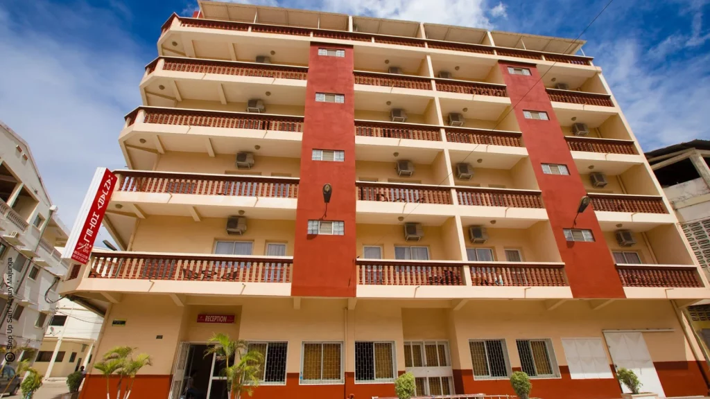 Façade extérieure du bâtiment de Anjary Hôtel avec balcons, situé en plein centre-ville de Majunga sous un ciel bleu.