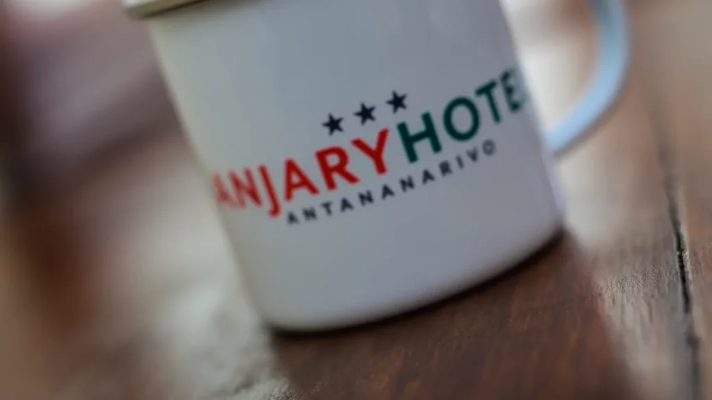 Tasse blanche en émail affichant le logo aux trois étoiles de l'Anjary Hôtel, établissement de référence à Antananarivo